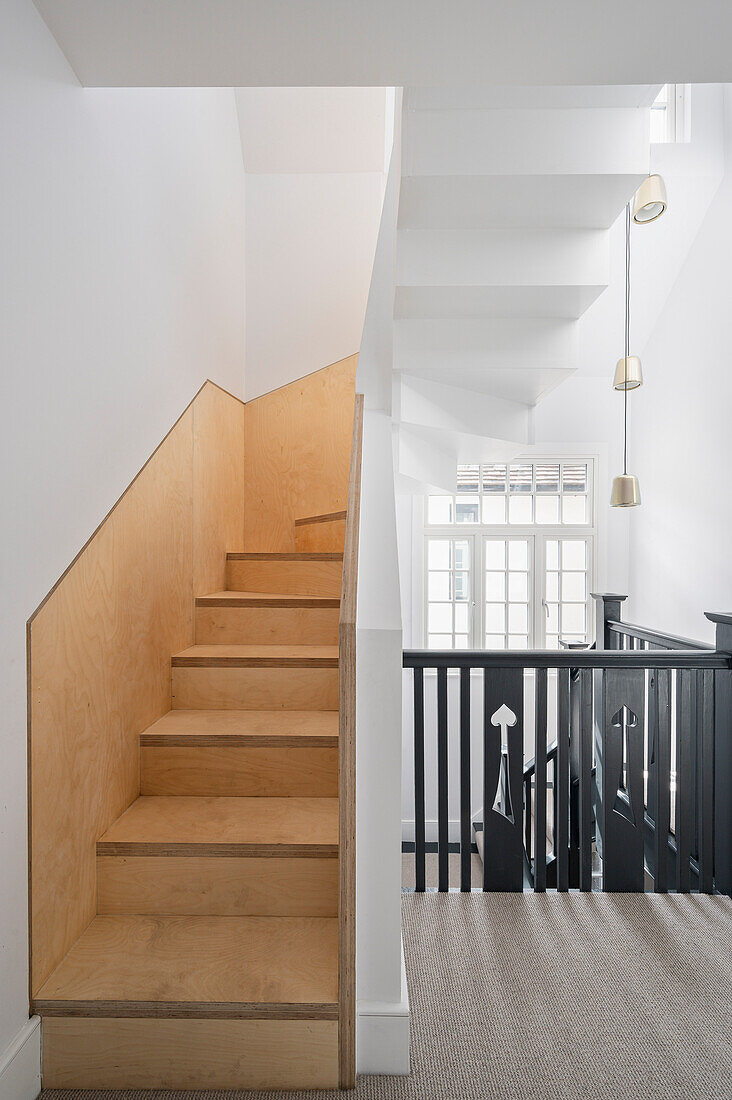Weißes Treppenhaus mit Holztreppen und schwarzem Geländer