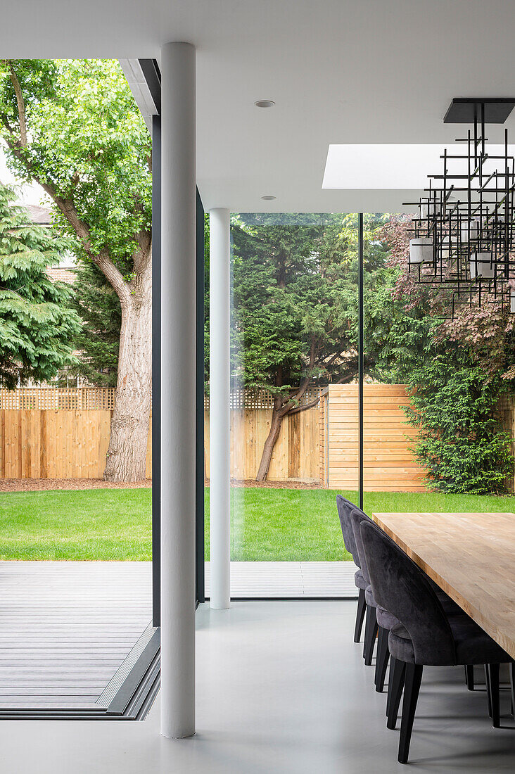 Esstisch aus Holz mit gepolsterten Stühlen vor Fensterfront mit Gartenblick