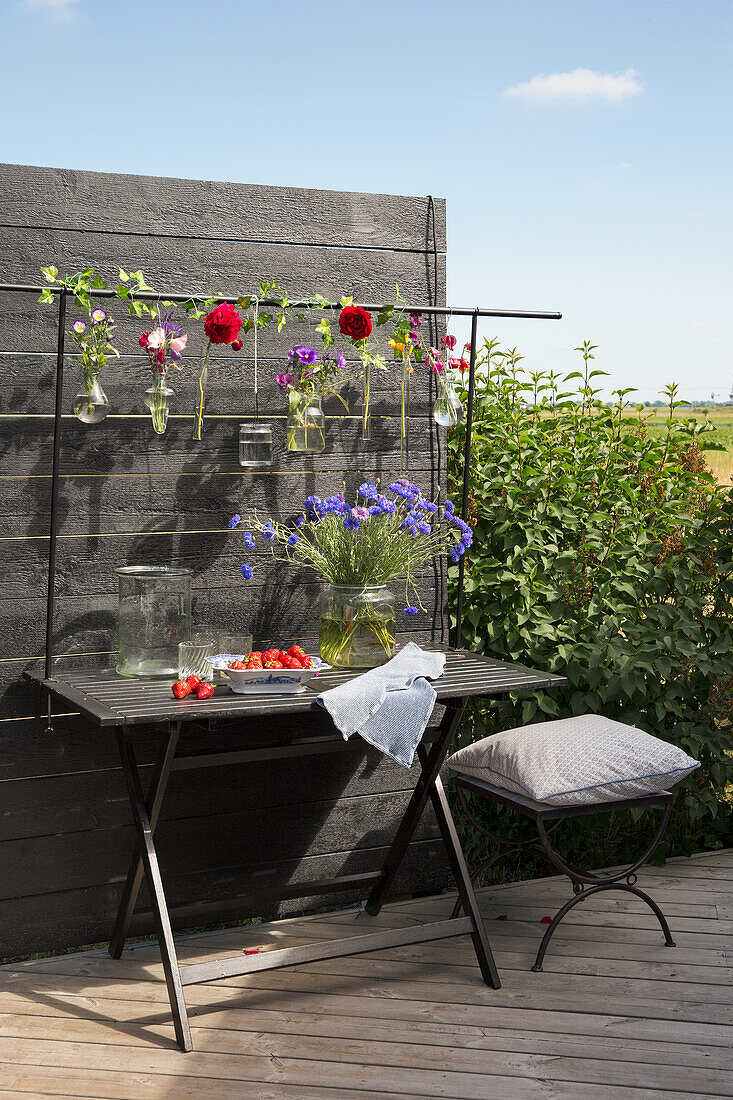 Hanging vases with various flowers above table on a terrace
