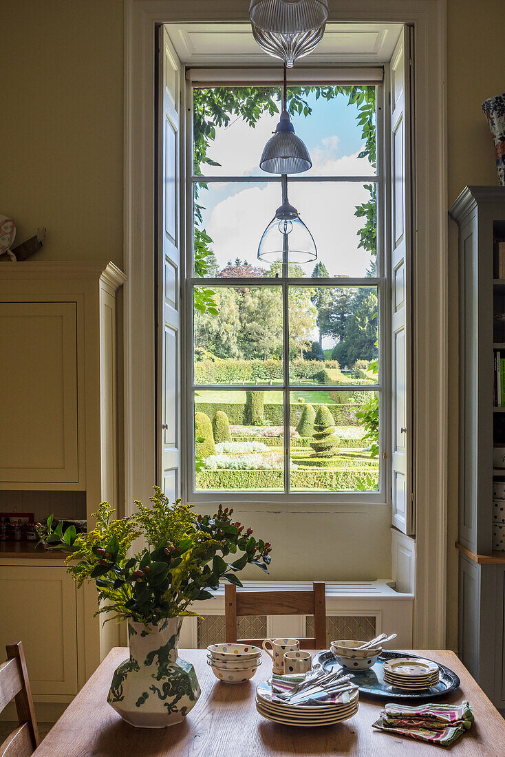 Vase mit Schnittblumen und Geschirr auf Tisch, Blick auf parkähnlichen Garten