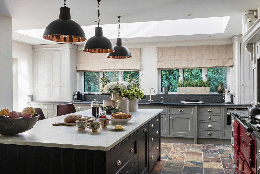 Custom made kitchen island, industrial style pendant lights above it in an open kitchen with colorful slate floor