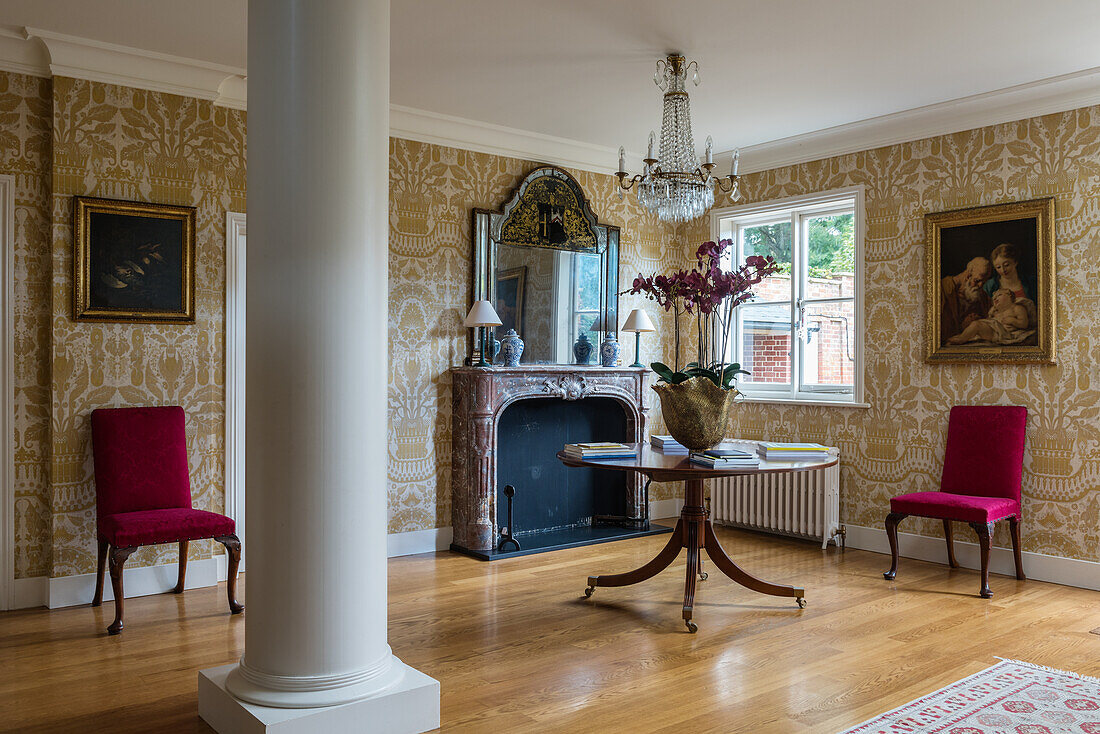 Round table with orchids in the wallpapered reception room with column in an English country house