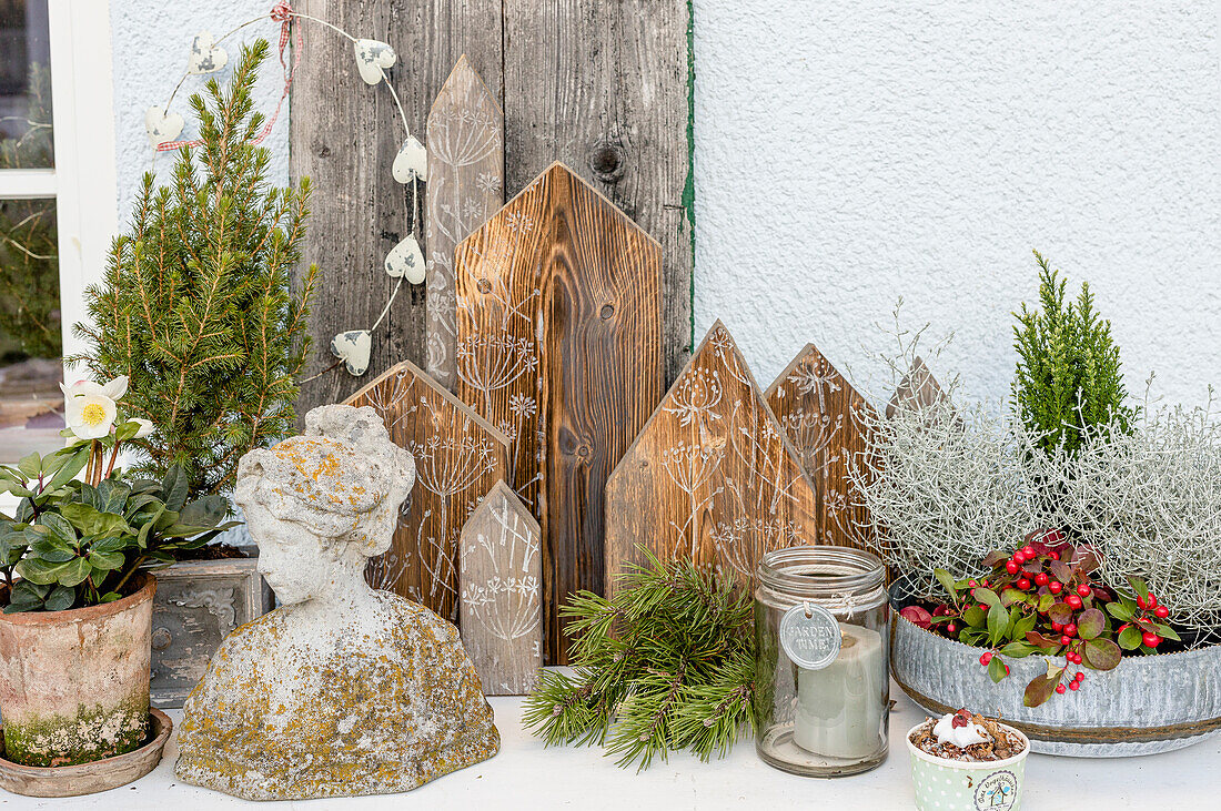 Winterliches Arrangement mit Pflanzen, Büste und Holzhäuschen auf der Terrasse