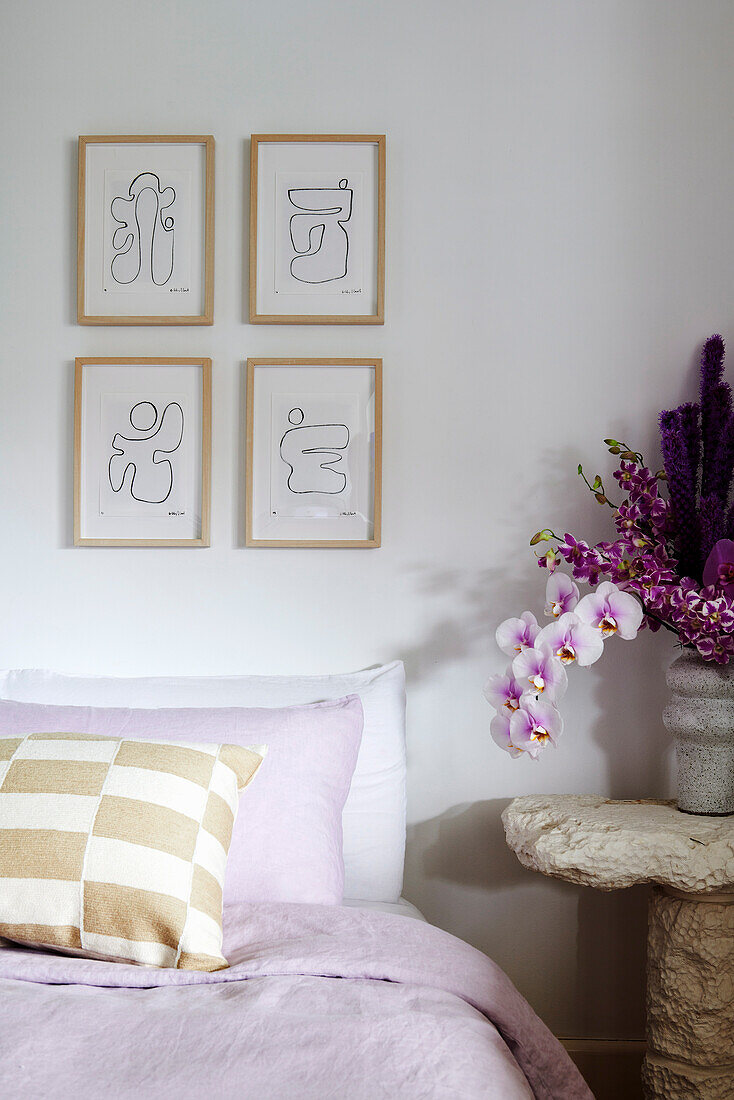 Bed with pillows, drawings above, bedside table with orchids