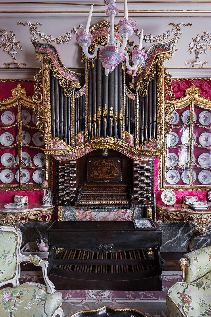 Orgel, umgeben von viktorianischen Wandtellern an der Wand mit himbeerfarbener Seide