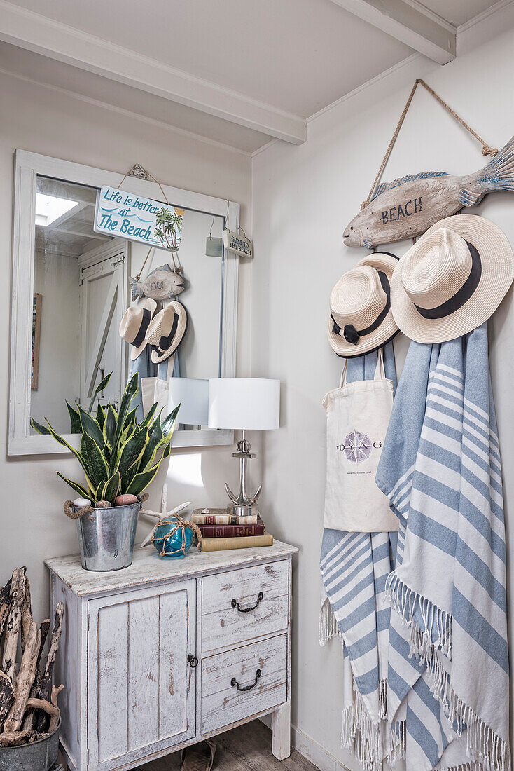 Driftwood fish as wall coat rack with sun hats and towels, wooden cabinet, and mirror in the hallway