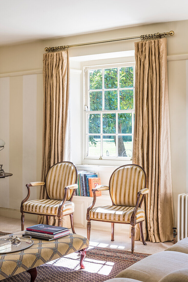 Antique style chairs in front of a window with floor length linen curtains in light living room
