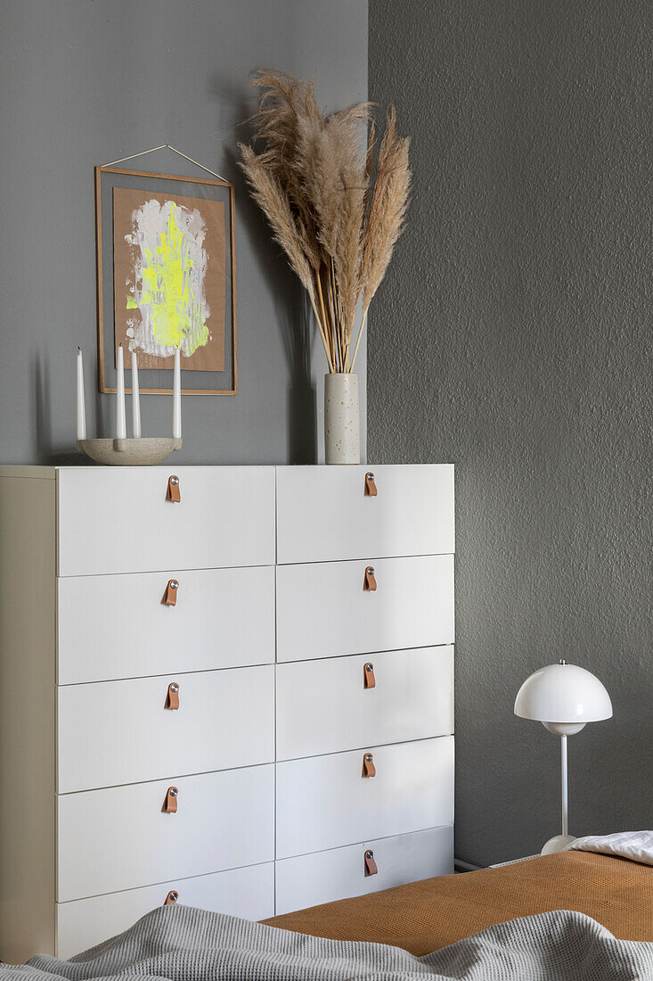 White chest of drawers with leather handles in the bedroom with grey walls