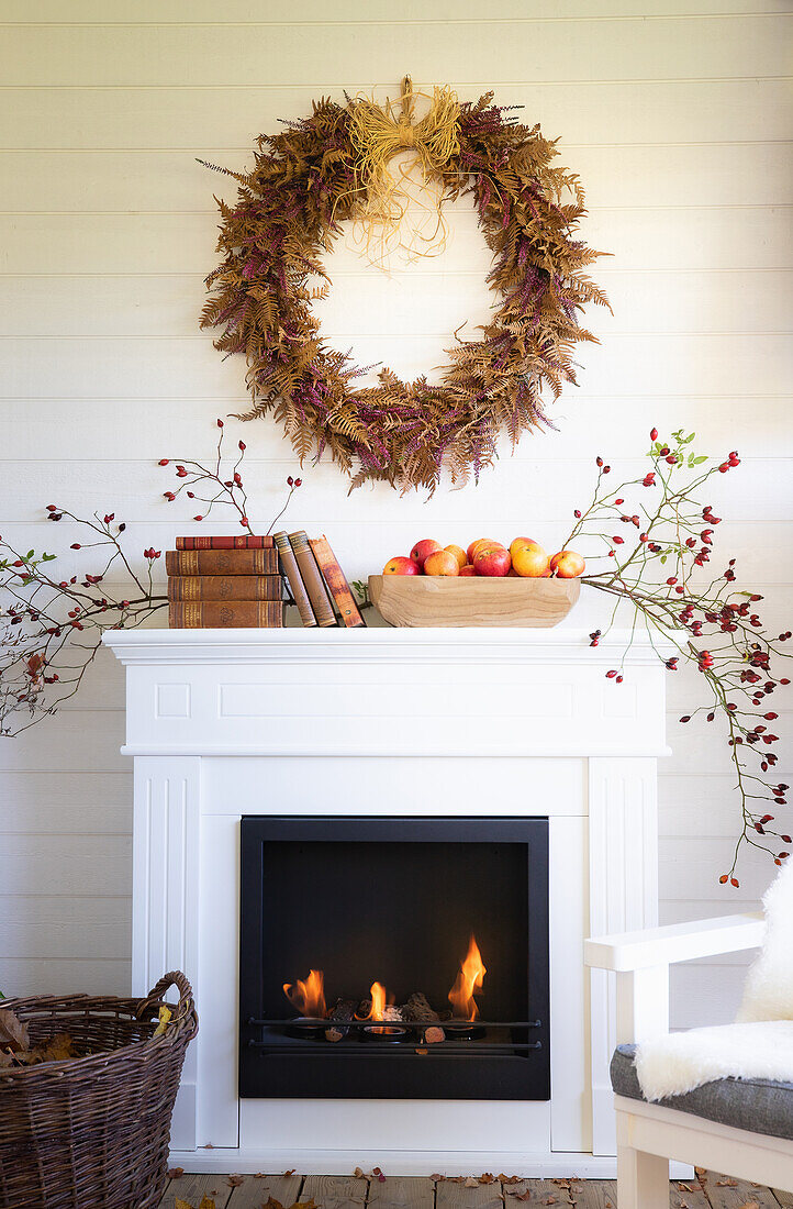 White fireplace with fire, above it autumn wreath on the veranda