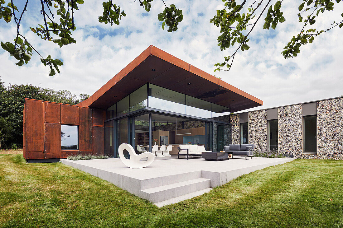 Großzügige Terrasse mit Sitzmöbeln vor Architektenhaus aus Glas und Cortenstahl