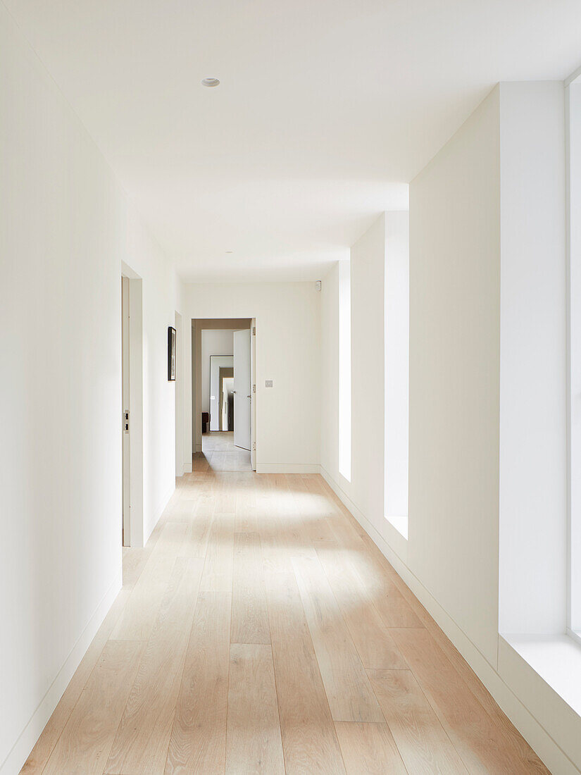White hallway with windows and light wooden floor