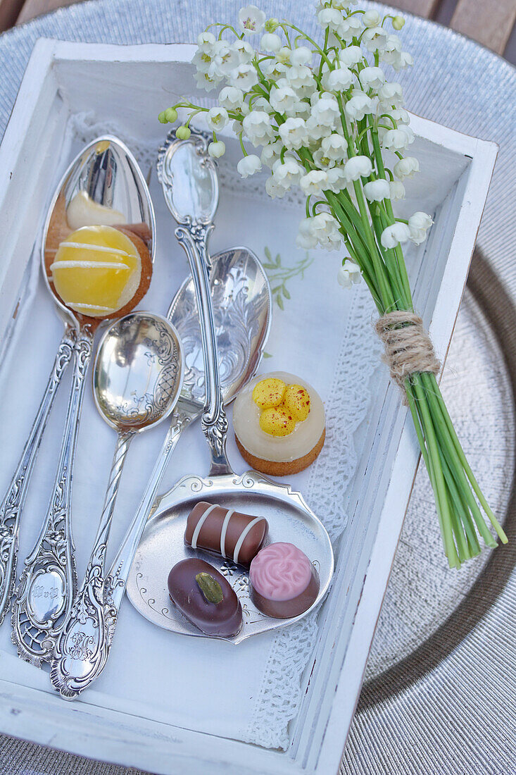 Chocolates with silverware and lily of the valley on a wooden tray