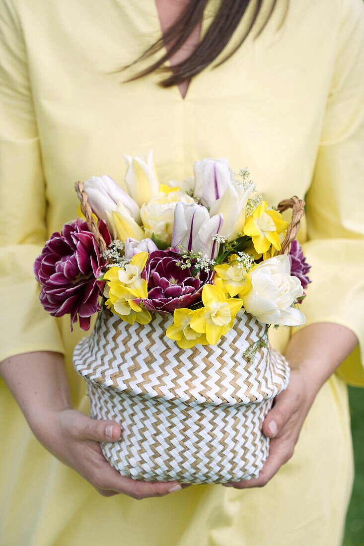 Frau in gelbem Kleid hält einen Korb mit bunten Frühlingsblumen