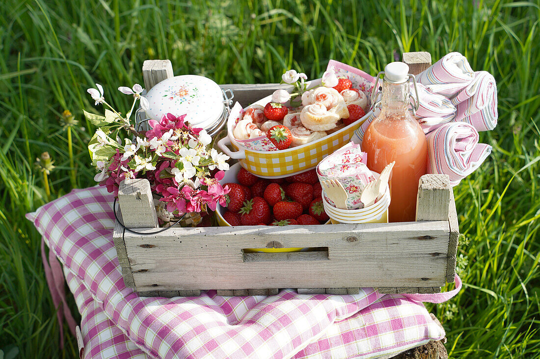 Picknickkorb mit Erdbeeren, Getränk und Blumen auf Wiese