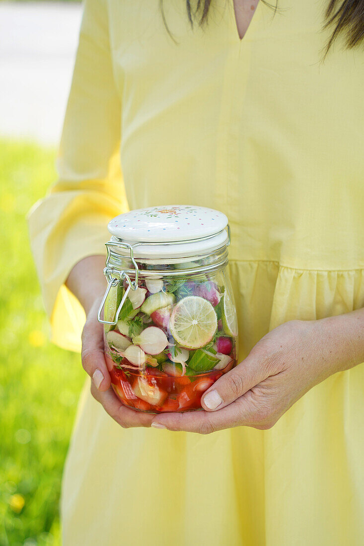 Woman in yellow dress holding jar with vegetables and lemon slices