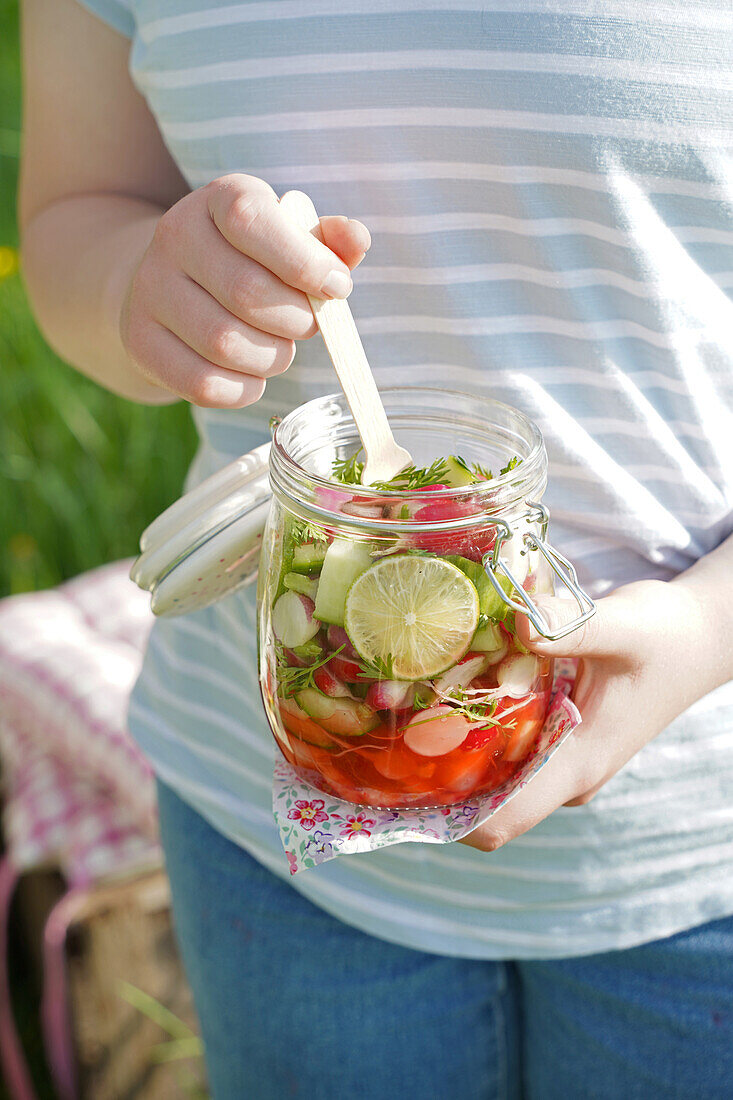 Preserving jar with fresh vegetable snack and wooden fork outdoors