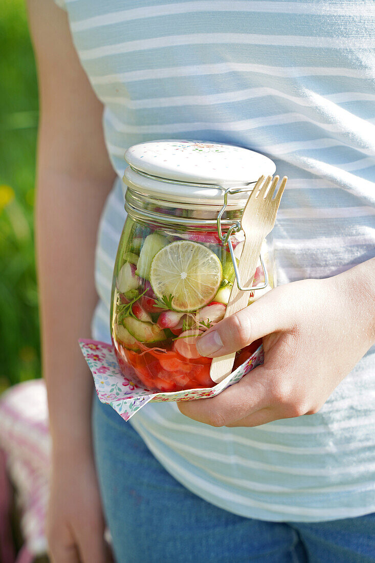 Einmachglas mit frischem Salat und Gabel in der Hand einer Person im Freien