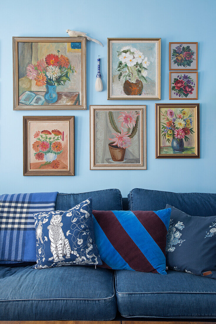 Blaues Sofa mit Denim-Bezug und Kissen, darüber Bildergalerie im Wohnzimmer mit hellblauer Wand