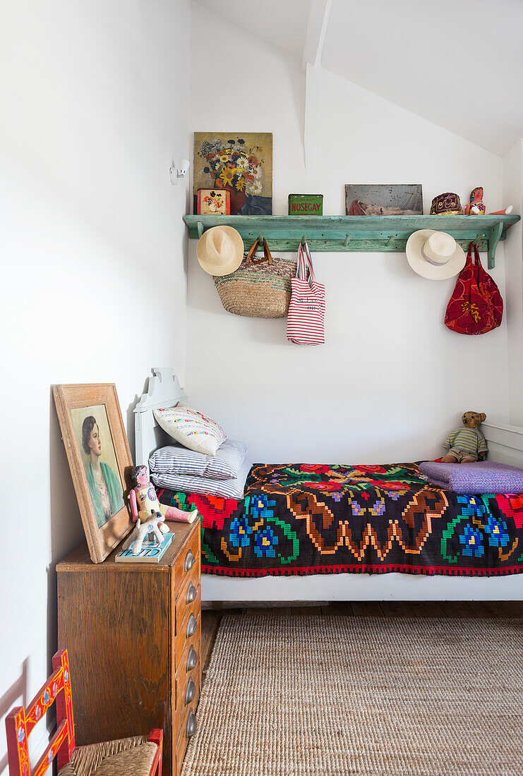 Bed with colorful bedspread, above it green shelf in white painted guest room