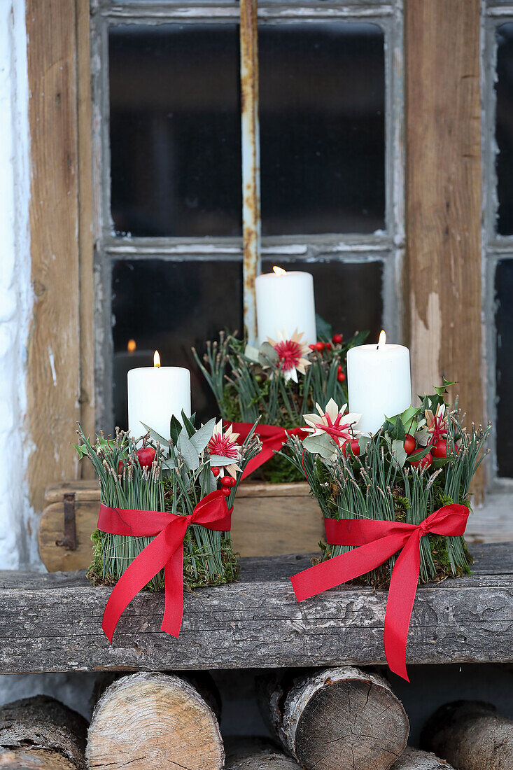 Christmas candle decorated with red bows on a wooden bench in front of a window