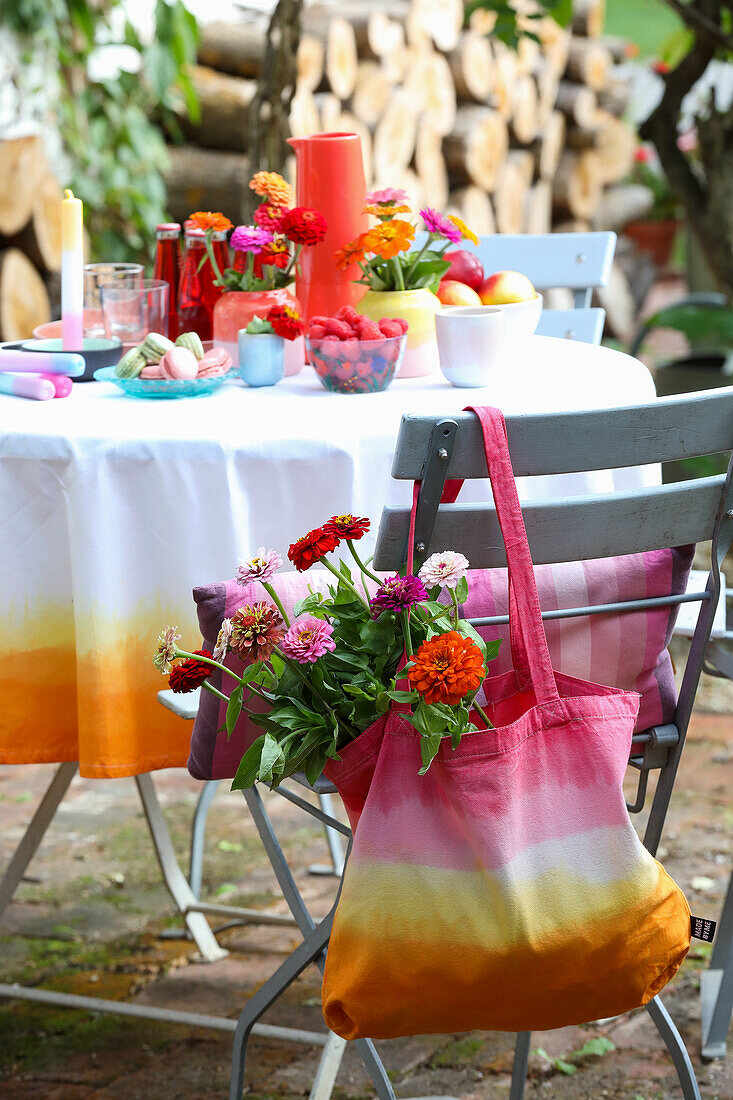 Bunte DIY-Stofftasche mit Dahlien an Stuhllehne und Sommertisch im Garten