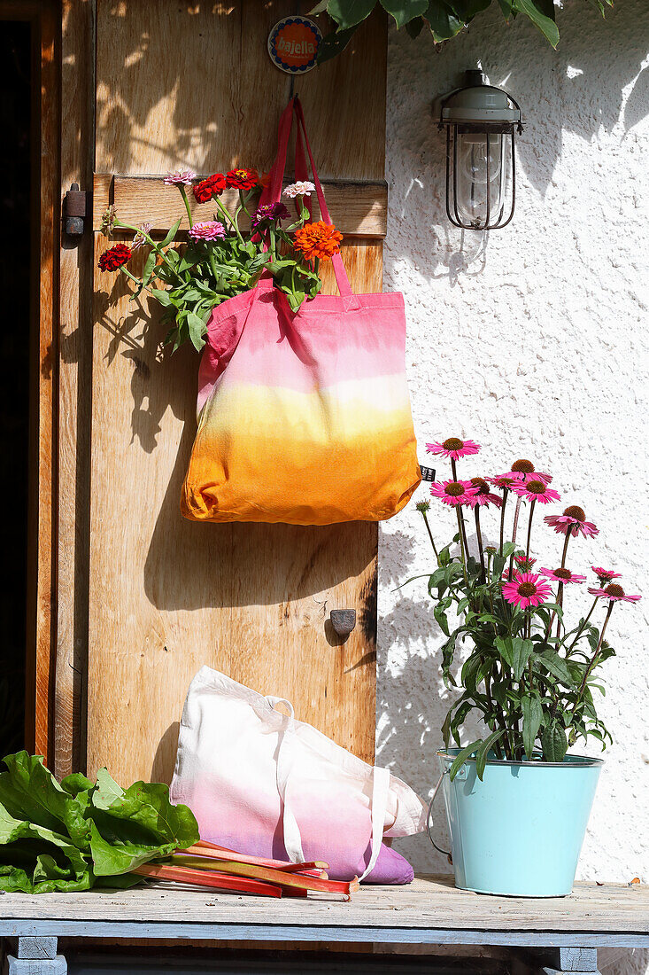 Bunte DIY-Stofftasche mit Dahlien an Holztür, davor Purpur-Sonnenhut im Topf