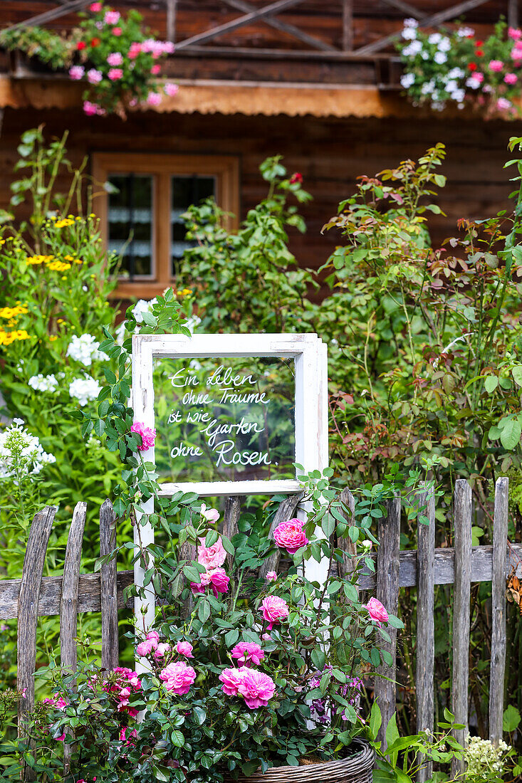 Sommergarten mit Rosen, altes Fenster mit Botschaft am Zaun