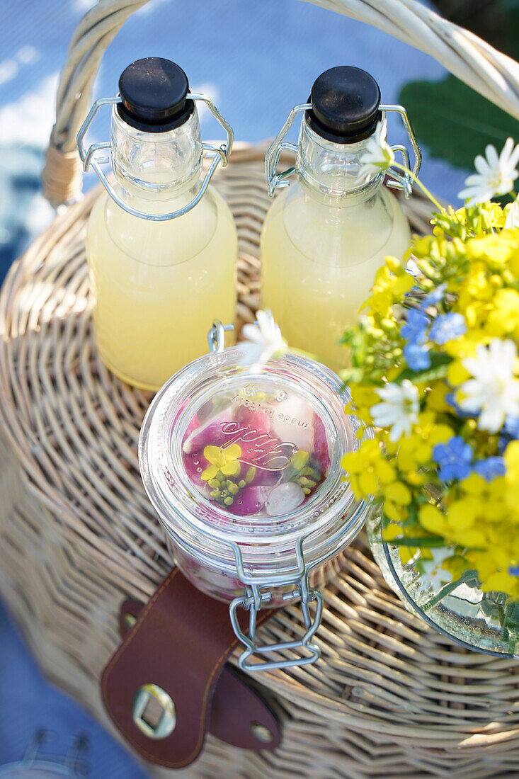 Zwei Flaschen mit Limonade und Blumenstrauß im Weidenkorb