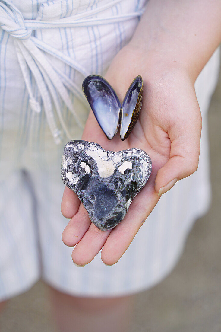 Hand holding heart-shaped stone and open mussel shell