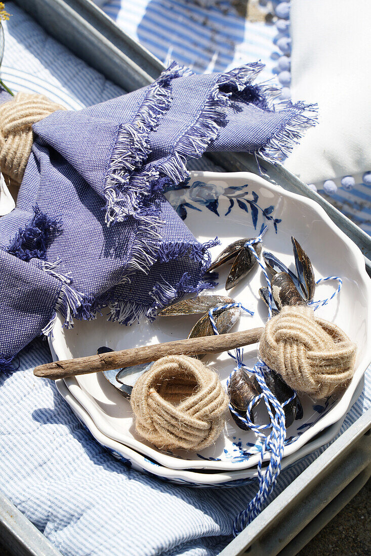 Maritime decor with napkin rings, driftwood and mussel shells on blue and white crockery