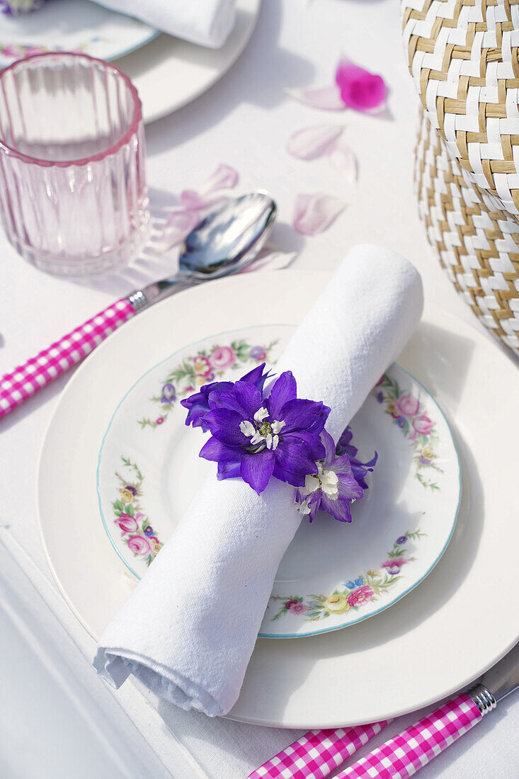 Place setting with napkin ring made of purple flowers and cutlery with checkered handles