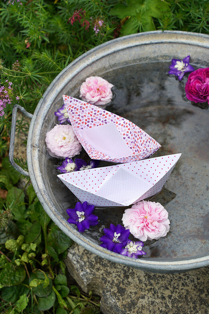 Paper boats and floating flowers in a zinc tub filled with water in the garden