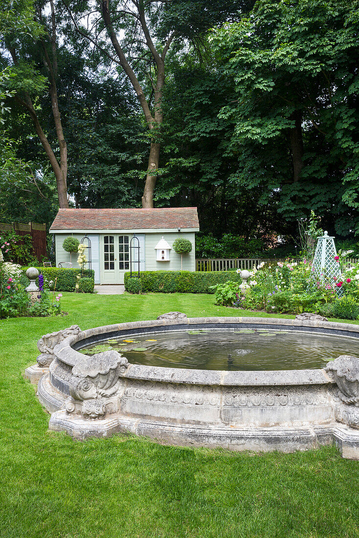 Antique pond in a well kept garden, summer house in the background