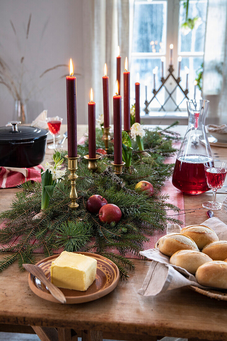 Festive wooden table with red candles, fir branches and apples