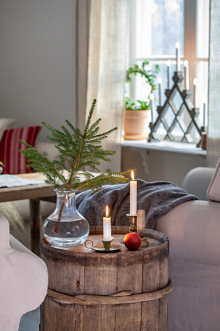 Dekorierter Wohnbereich mit Holzfass, Kerzen und Tannenzweig im Glas