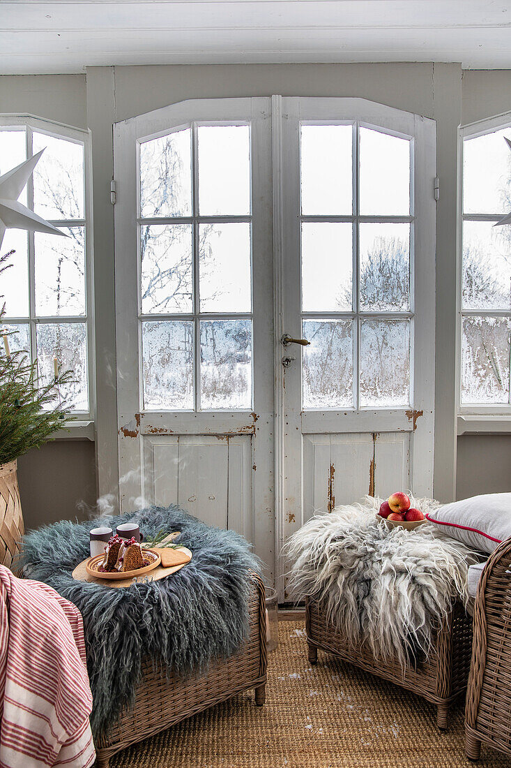 Wintergarten mit zwei geflochtenen Sesseln und Fellüberwürfen