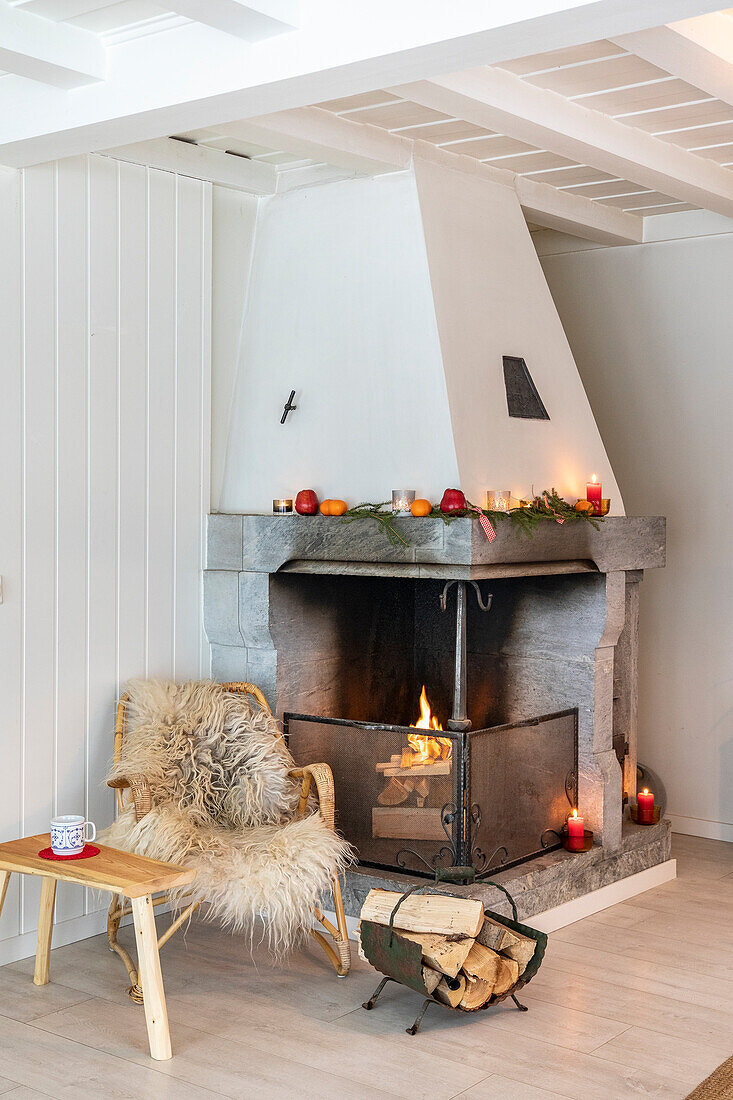 Fireplace with cosy seating area with wooden chair and fur in a living room decorated for Christmas