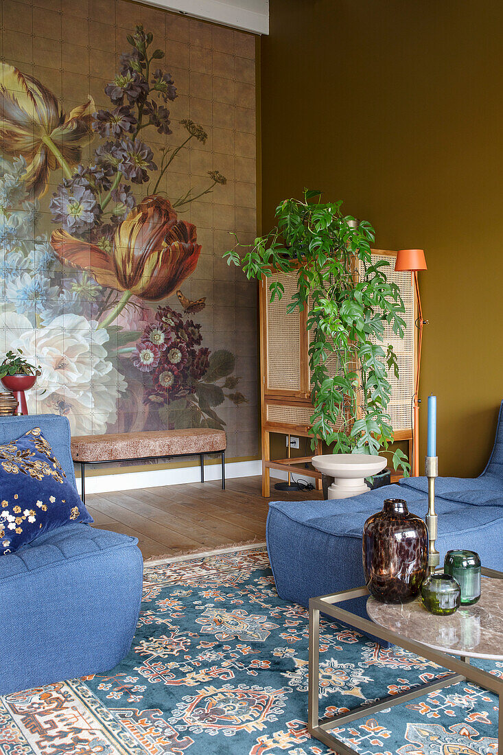 Living room with botanical wallpaper, rattan cupboard, blue armchairs and oriental rug