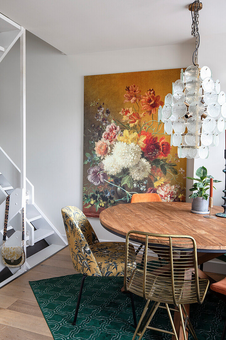 Dining area with round wooden table, large flower painting on the wall and modern chandelier