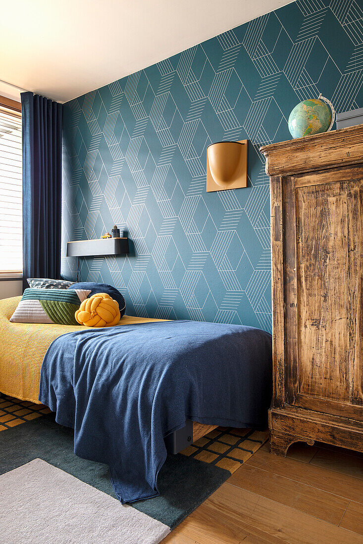 Bed with blue bedspread and modern, geometric wallpaper in the bedroom