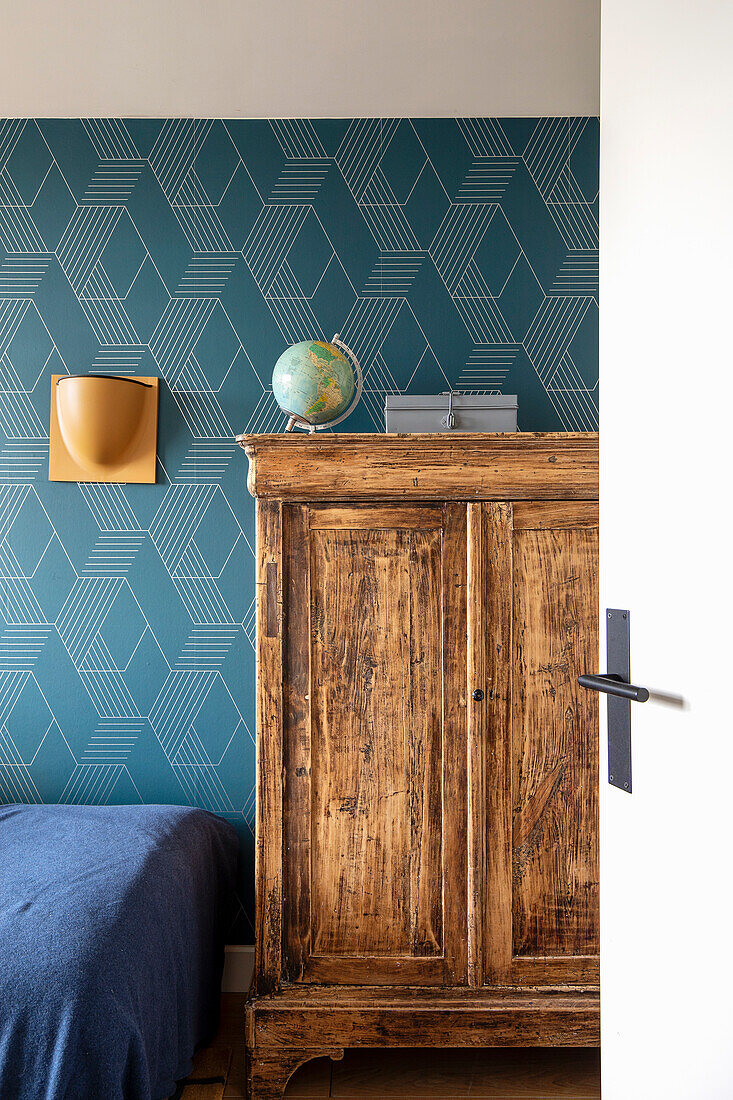 Wooden cupboard in front of geometrically patterned wallpaper in the bedroom