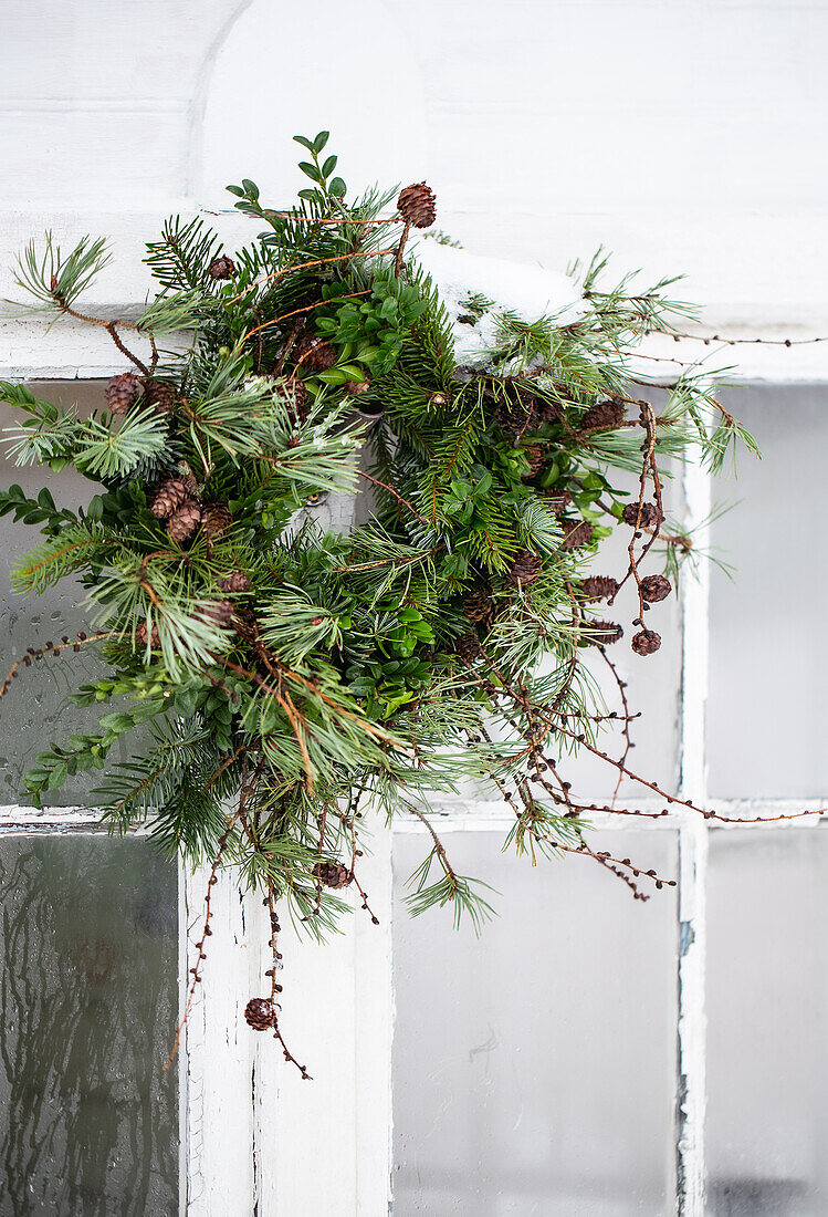 Door wreath made of twigs and cones on a white window