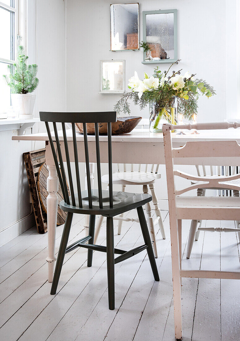 Dining room with white wooden table and mixed chairs, bouquet of flowers