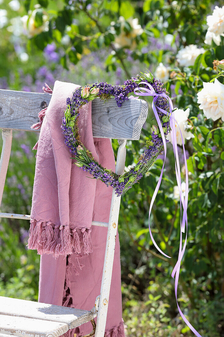 Lavendel-Herzkranz und rosa Tuch hängen an Gartenstuhl im Sommergarten