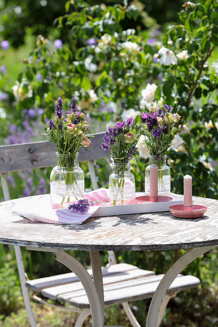 Runder Holztisch im Garten mit Blumensträußen in Glasvasen und Kerzen