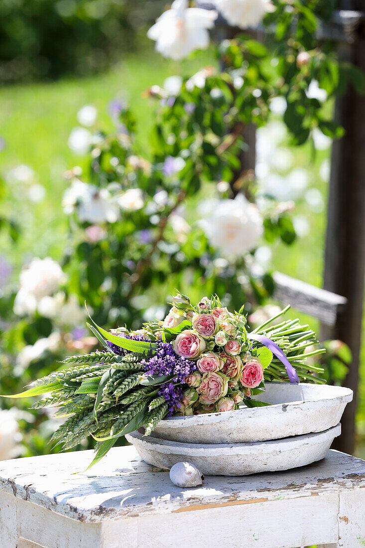 Blumenstrauß mit Rosen (Rosa), Lavendel (Lavandula) und Getreideähren auf Holztisch im Garten