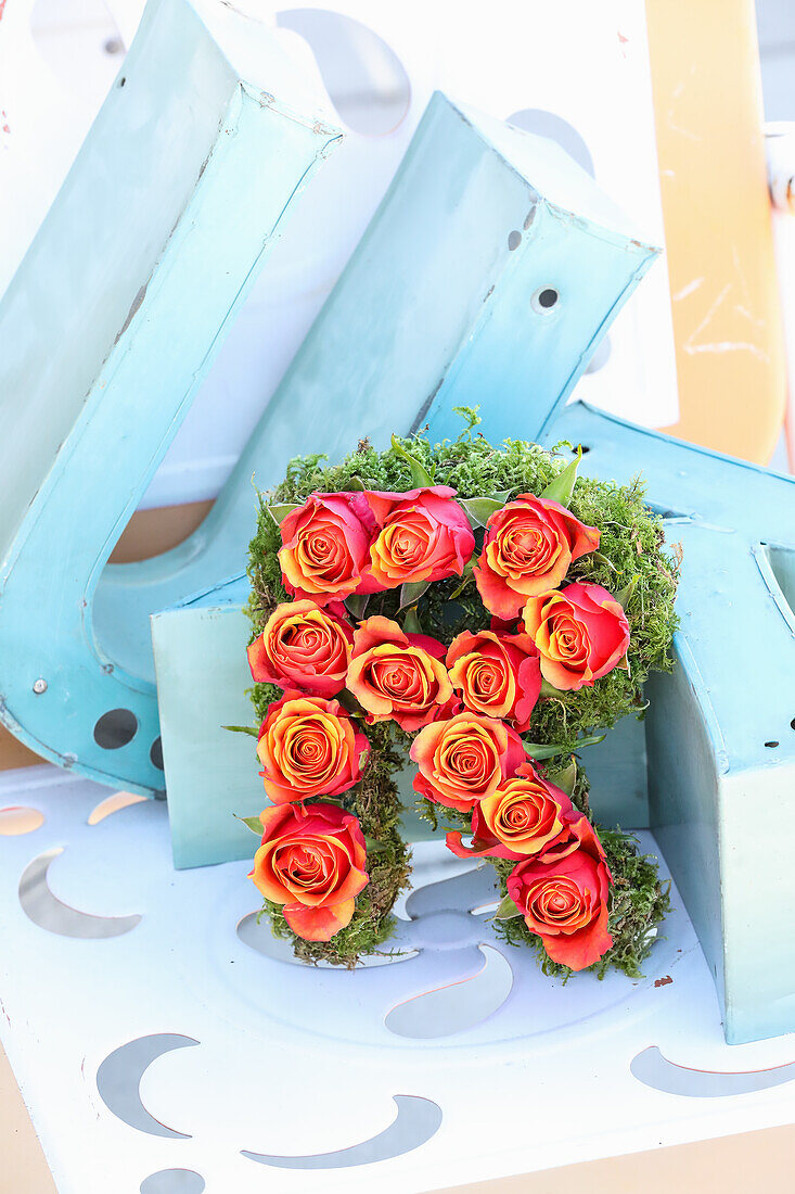 Letter "R" made of roses and moss, decoration on light blue metal background