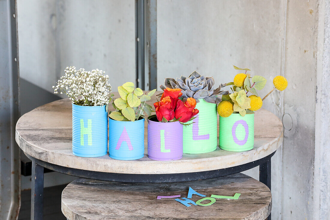 Colourful tin cans with flowers result in "HELLO" lettering on wooden table