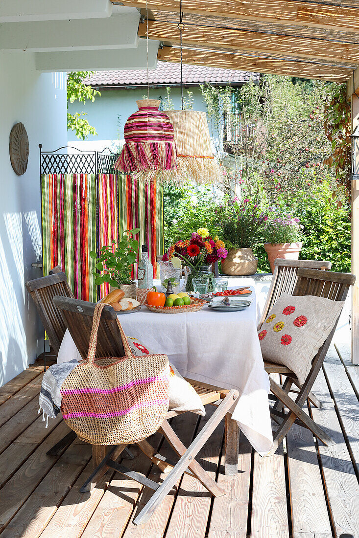 Gedeckter Holztisch auf überdachter Terrasse mit bunter Sommerdeko