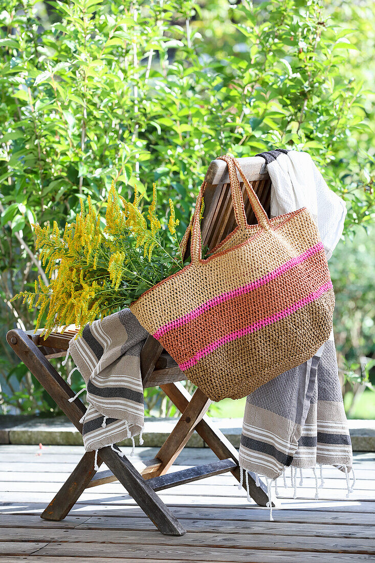 Gartenstuhl mit gestreifter Decke und geflochtener Tasche voller Goldruten (Solidago)